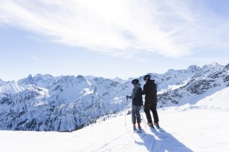 Zwei Skifahrer halten am Rand der Piste inne und lassen den Blick über die beeindruckende Winterlandschaft schweifen.