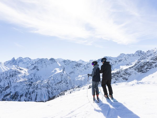 Zwei Skifahrer stehen heute am Pistenrand und genießen den weiten Blick über die verschneiten Alpen. Zwei Skifahrer halten am Rand der Piste inne und lassen den Blick über die beeindruckende Winterlandschaft schweifen.