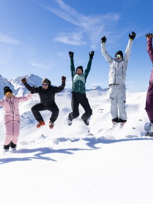 Sechs Freunde springen gemeinsam in die Luft und feiern ihren Wintertag vor der eindrucksvollen Bergkulisse.