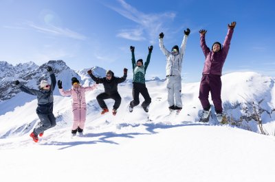 Sechs Freunde springen jubelnd im Schnee vor sonnigem Bergpanorama und blauem Himmel bei Oberstdorf. Sechs Freunde springen gemeinsam in die Luft und feiern ihren Wintertag vor der eindrucksvollen Bergkulisse.