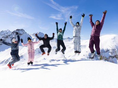 Sechs Freunde springen gemeinsam in die Luft und feiern ihren Wintertag vor der eindrucksvollen Bergkulisse.