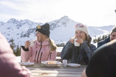 Heiße Tassen, Wintersonne und beste Stimmung: Zwei Freundinnen genießen ihre gemeinsame Pause am Berg.
