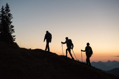 Drei Wanderer als Silhouetten bei Sonnenaufgang auf einem Berggrat Drei Wanderer sind bei Sonnenaufgang als Silhouetten auf einem Berggrat zu sehen.