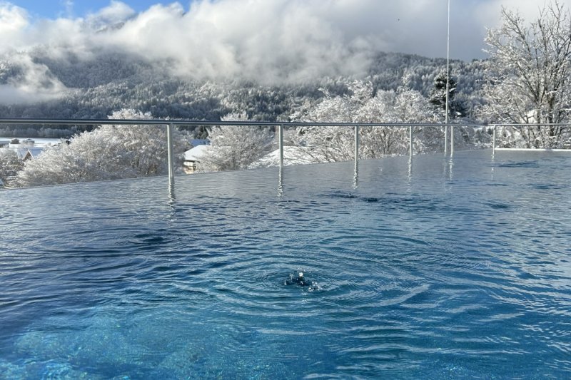 Blick über den Infinity-Pool mit verschneiten Bergen und Wolken im Hintergrund bei traumhaften Wetter.