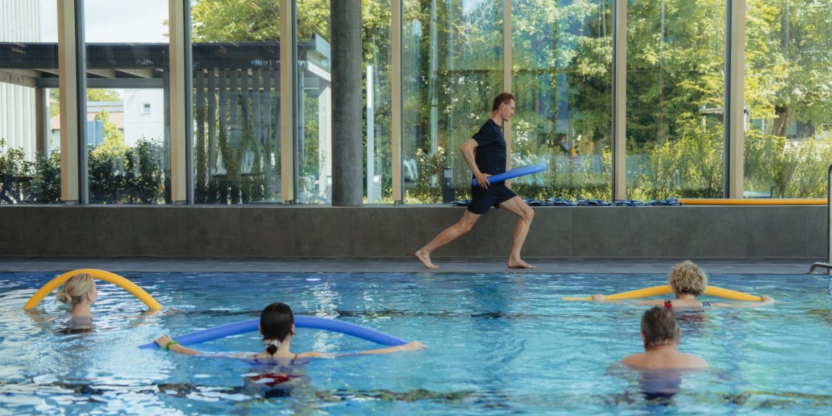 Mehrere Personen sind im Schwimmbecken, die gemeinsam Aquafittness machen.