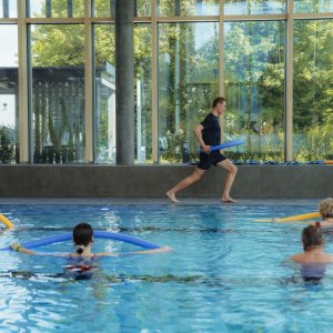 Mehrere Personen sind im Schwimmbecken, die gemeinsam Aquafittness machen.