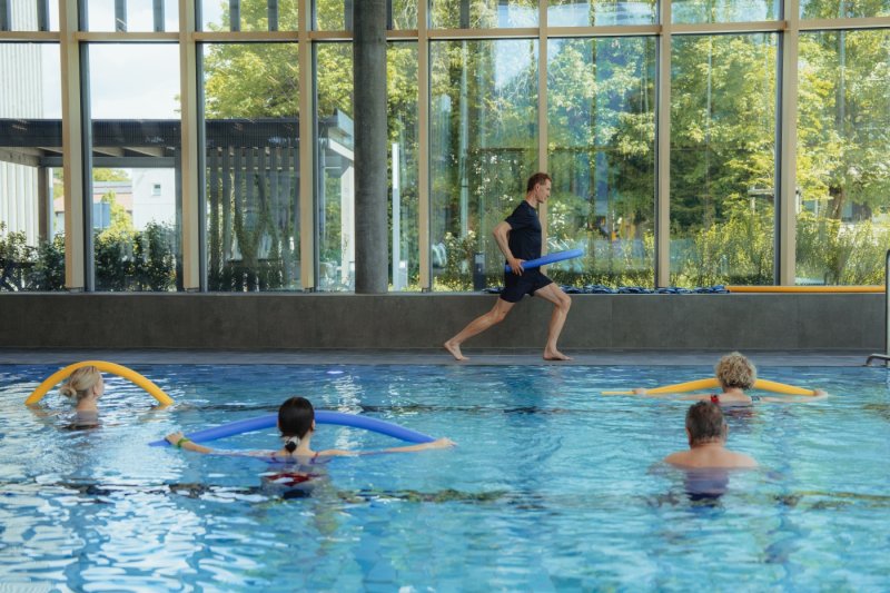 Mehrere Personen sind im Schwimmbecken, die gemeinsam Aquafittness machen.