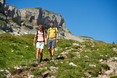 Ein Paar wandert an einem sonnigen Tag auf einem Bergweg. Die Landschaft ist grün und majestätisch.