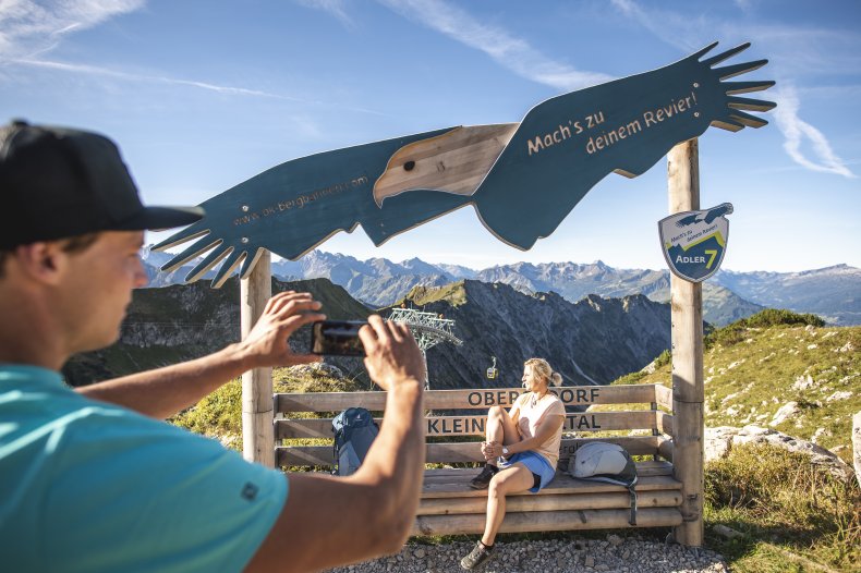 Tolle Aussicht am Fotopunk Ein Mann macht ein Foto von einer Frau mit Bergen im Hintergrund an einem klaren, sonnigen Tag in den Alpen.
