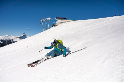 Ein Skifahrer gleitet geschmeidig über die schneebedeckte Piste in den Bergen bei klarem Himmel und Sonnenschein.