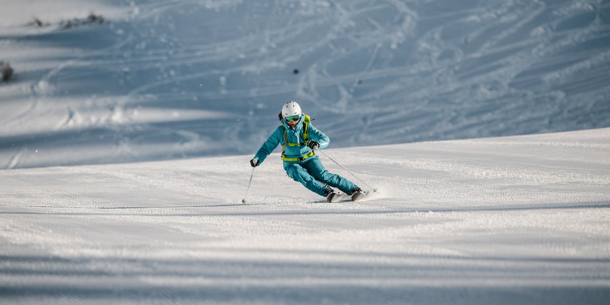 Ein Skifahrer fährt schnell über die schneebedeckte Piste an einem klaren Wintertag in den Bergen.