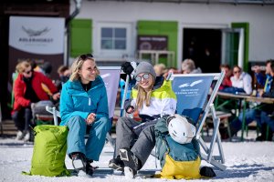 Sonne tanken am Adlerhorst Zwei Frauen genießen die Sonne auf einer Skipiste, während sie sich zwischen Pistenbesuchen entspannen und unterhalten.