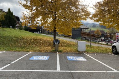 E-Ladestation Kanzelwand Zwei behindertengerechte Stellplätze auf einem Parkplatz, umgeben von buntem Herbstlaub und einer ruhigen Landschaft in den Bergen.