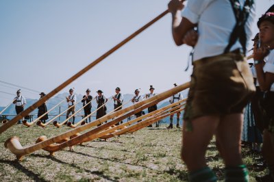 Berglar-Kirbe am Fellhorn Gruppen von Menschen spielen Alphörner in den Bergen unter klarem Himmel. Die Veranstaltung findet tagsüber statt.