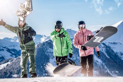 Drei Snowboarder fahren auf frischem Schnee und zeigen beeindruckende Tricks in den Bergen bei klarem Wetter.