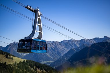 Eine Seilbahn schwebt über die Alpenlandschaft bei klarem Wetter, umgeben von hohen Bergen und grünen Wiesen.