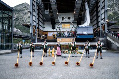 Sechs Musiker mit Alphörnern stehen auf dem Platz vor der Bergbahnstation und spielen traditionelle Musik.