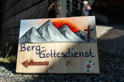 Ein Schild weist den Weg zum Berggottesdienst in den Alpen bei Sonnenuntergang. Die ruhige Atmosphäre lädt zum Nachdenken ein.