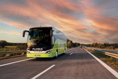 Mit dem FlixBus in die Berge | ein grüner Bus mit der Aufschrift FlixBus fährt auf der Autobahn. Der Himmel zeigt ein rot-blau im Sonnenuntergang.