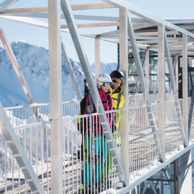 Zwei Skifahrer stehen auf einer Aussichtsplattform in den Alpen und genießen die spektakuläre Aussicht auf die schneebedeckten Berge.