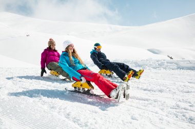 Mit Freunden im Schnee Drei Personen rodeln im Schnee an einem sonnigen Tag in den Bergen. Die Landschaft ist schneebedeckt und klar.