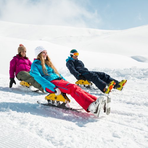 Mit Freunden im Schnee Drei Personen rodeln im Schnee an einem sonnigen Tag in den Bergen. Die Landschaft ist schneebedeckt und klar.