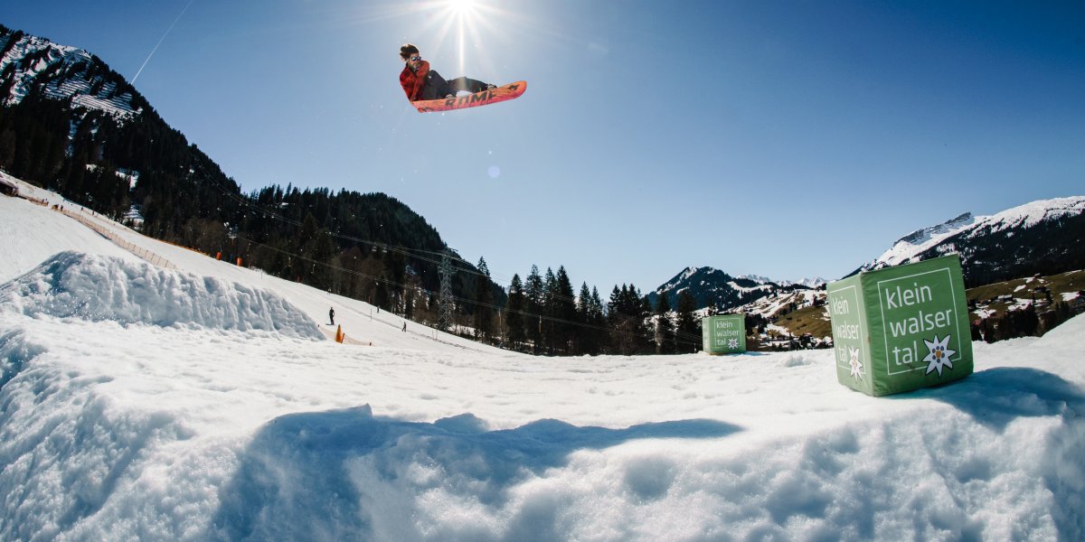 Snowboard Crystal Ground 7@eignerphoto Ein Snowboarder macht einen Sprung über eine Schneegrube im Kleinwalsertal an einem sonnigen Tag im Winter.