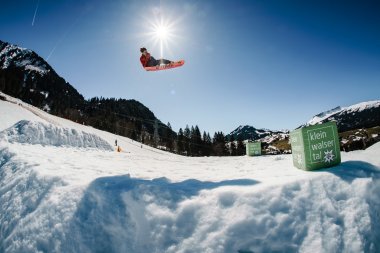 Ein Snowboarder macht einen Sprung über eine Schneegrube im Kleinwalsertal an einem sonnigen Tag im Winter.