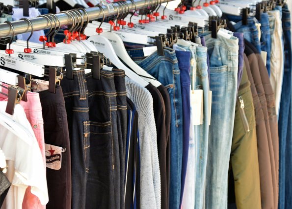 Im Geschäft sind viele Hosen auf einem Ständer aufgehängt. Kunden schauen sich die Auswahl an und prüfen die Größen.