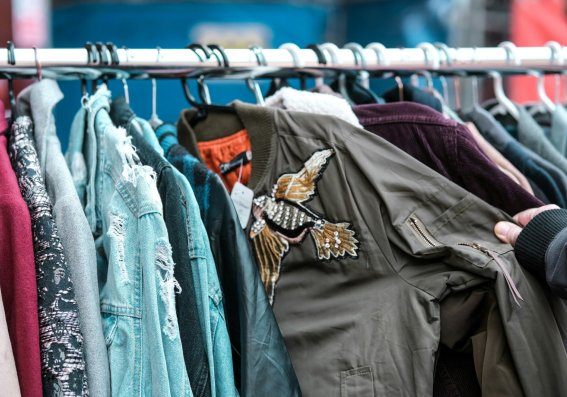Eine Person schaut sich Jacken auf einem Marktstand an. Die Jacken sind in verschiedenen Farben und Stilen.