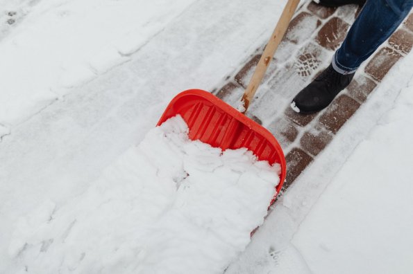 Schneeräumen auf dem Weg im Winter Eine Person schaufelt Schnee auf einem Gehweg. Es ist Winter, der Boden ist weiß. Die Person trägt warme Kleidung und Stiefel.
