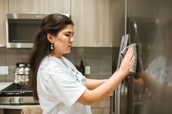 Frau reinigt den Kühlschrank in der Küche Eine Frau wischt den Kühlschrank in einer modernen Küche mit einem Tuch sauber. Sie ist konzentriert bei der Arbeit.