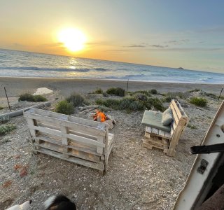 Am Strand genießen Menschen einen Sonnenuntergang. Palettenmöbel bieten Komfort während der Abendstunden.