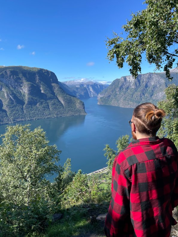 Eine Wandererin genießt den herrlichen Ausblick auf den Fjord in Norwegen an einem sonnigen Tag. Die umliegenden Berge sind beeindruckend.