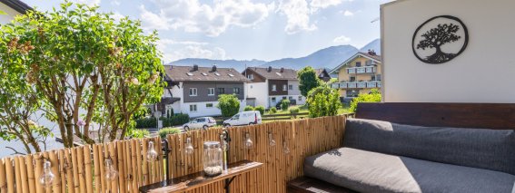 Auf dem Balkon steht eine Couch aus Paletten. Die Sonne scheint, und die Umgebung ist von Wohnhäusern umgeben.