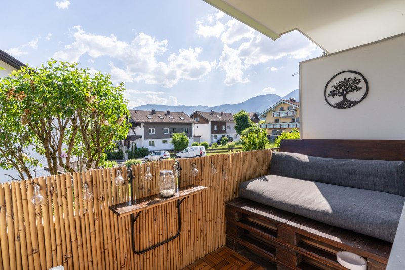 Auf dem Balkon steht eine Couch aus Paletten. Die Sonne scheint, und die Umgebung ist von Wohnhäusern umgeben.