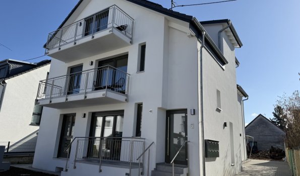 Modernes Haus in einer ruhigen Nachbarschaft Ein großes, modernes Haus mit Balkonen und einem hellen Himmel. Es steht in einer ruhigen Straße mit anderen Häusern.