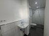 Der Raum zeigt eine minimalistischen Gestaltung mit einer Dusche, Waschbecken und Toilette.