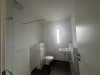 In einem kleinen Badezimmer gibt es eine Toilette, ein Waschbecken und viel helles Licht von einem Fenster.