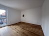 In einem leeren Raum stehen Wände und Holzfußboden bereit. Ein Fenster öffnet sich nach draußen.