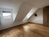 Der Raum hat einen Holzfußboden, ein Fenster und helle Wände. Es gibt keinen sichtbaren Möbelstück.