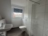 In einem modernen Bad sind eine Dusche und eine Toilette zu sehen. Der Raum hat eine große Fensterfront.
