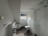 Das Badezimmer zeigt eine Dusche, eine Toilette und ein Waschbecken. Es hat ein Fenster und helle Wände.
