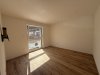 In einem leeren Zimmer steht ein Fenster. Der Boden ist aus Holz. Es gibt Tageslicht.