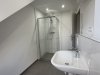 Das Badezimmer zeigt eine Dusche und ein Waschbecken. Es ist hell und modern, mit gefliesten Wänden und Boden.