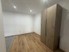 Der Raum hat einen Holzfußboden. Ein Schrank steht an der Wand. Es gibt keine Möbel und viele Lichtquellen.