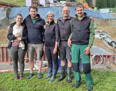 Familie Holzmann steht vor der Baustelle, die Bodenplatte wurde betoniert