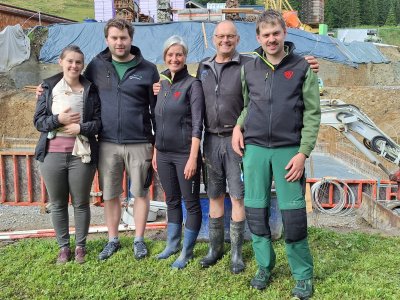 Familie Holzmann steht vor der Baustelle, die Bodenplatte wurde betoniert