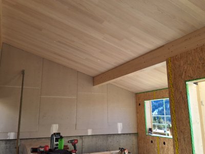 Der Raum zeigt eine schlichte Holzdecke mit sichtbaren Balken. Handwerker arbeiten am Bau in einem hellen, offenen Bereich.