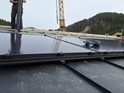 Arbeiter montieren Solarpanels auf dem Dach eines Gebäudes in den Bergen während eines klaren Tages.